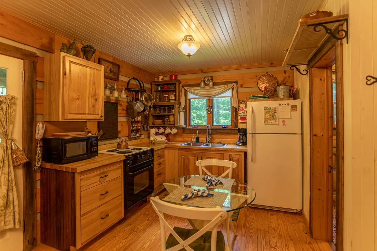 A well-lit kitchen and dining area showcasing modern appliances, wooden cabinetry, a glass dining table, and a window letting in natural light. The space looks fully equipped and ready for cooking, serving as the heart of home-cooked meals and family stories, with a friendly, inviting atmosphere.