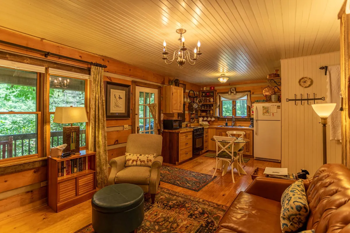 This image captures a bright, open-plan living area with a comfortable sofa, wooden cabinetry, a welcoming dining area, and large windows allowing natural light to flood the space. The layout clearly connects the living, dining, and kitchen areas, emphasizing the sense of togetherness. The visible decor suggests warmth and comfort, with ample seating for guests to gather.