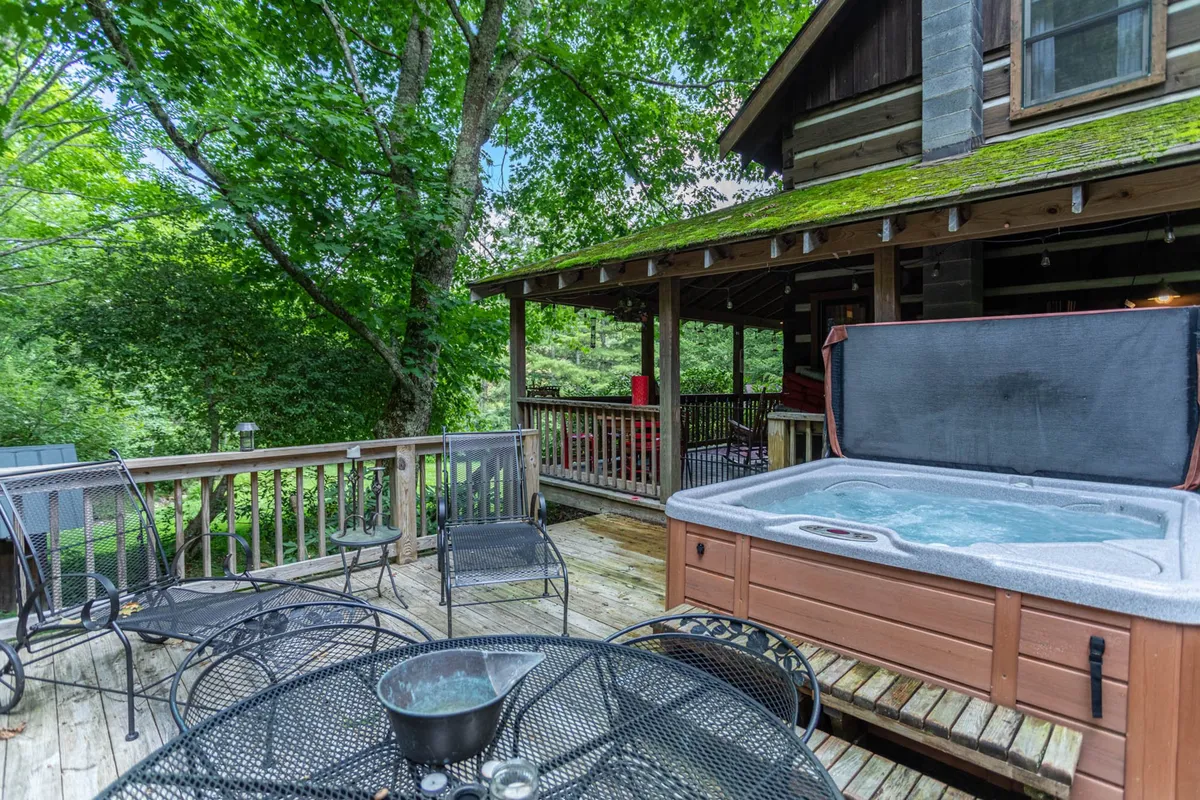 A wooden deck featuring a private hot tub and comfortable outdoor seating, surrounded by forested scenery. The setting is intimate, inviting couples to relax together while immersed in nature.
