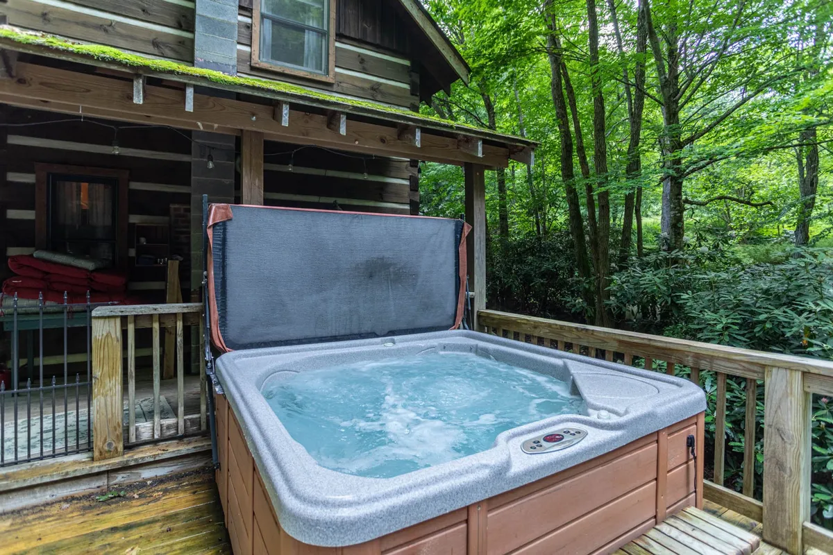 This image captures the cabin's spacious wooden deck with a bubbling hot tub, offering views of the surrounding trees and lush greenery. The inviting outdoor space is perfect for family relaxation, whether soaking in the hot tub, enjoying morning coffee, or gathering together for evening conversations.
